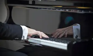 Dłonie muzyka w eleganckiej koszuli i garniturze grają najpiękniejsze utwory na fortepianie, tworząc magiczną melodię.