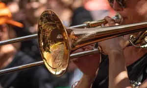 Muzyk w okularach gra na puzonie, tworząc dźwięki w stylu jazzowym.