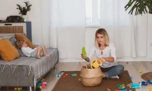Filip leży na kanapie, a mama, która chyba zapomniała o porządku, siedzi na dywanie wśród zabawek.