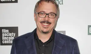 Vince Gilligan, twórca filmów, seriali i programów, w garniturze i okularach, uśmiecha się na tle logo "Film Society Lincoln Center" i symbolu pierwiastka "Br".