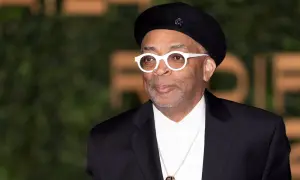 Spike Lee w czarnym beretce i białych okularach, od góry do dołu w czarnym garniturze i białej koszuli.