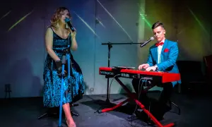 Wokalistka w niebieskiej sukience i pianista w garniturze tworzą duet. Ich występ to przykład kameralnych zespołów wokalnych.