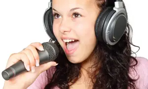 Młoda dziewczyna w słuchawkach śpiewa do mikrofonu. To popularny temat w muzyce jazzowej, uchwycony w radosnym momencie tworzenia.
