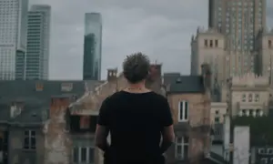 Młody mężczyzna z tatuażem "verte" na karku patrzy na panoramę Warszawy. Scena z serialu "Warszawianka".