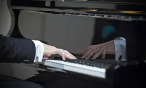 Dłonie w mankietach koszuli grają na fortepianie. W odbiciu widać drugiego pianistę. W tej chwili tworzą muzykę, jak prawdziwi sławni pianiści.