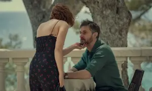 Kobieta w sukience w wiśnie dotyka brody mężczyzny. Napięcie między nimi sugeruje obsesję w tym serialu.