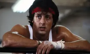 Spocony Rocky Balboa, z czerwoną opaską na głowie, opiera się o ring.