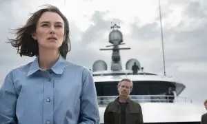 Kobieta z kabiny 10, w niebieskiej koszuli, stoi na tle luksusowego jachtu. W tle widać mężczyzn i chmury.