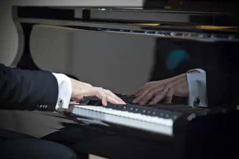 Dłonie muzyka w eleganckiej koszuli i garniturze grają najpiękniejsze utwory na fortepianie, tworząc magiczną melodię.