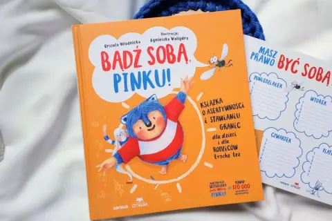 Pomarańczowa książka "Bądź sobą, Pinku!" z jeżem i zającem. Obok planer tygodniowy.