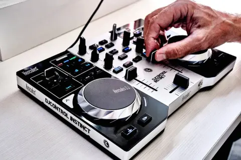 Dłoń DJ-a miksuje utwory na kontrolerze Hercules DJControl Instinct, tworząc energiczną muzykę do tańca.