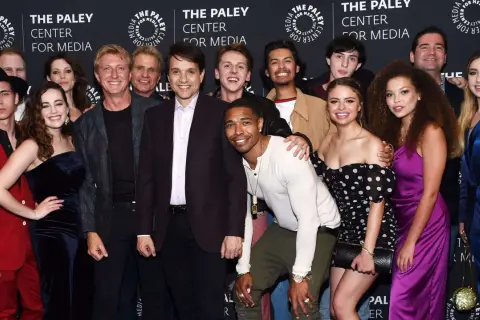 Uśmiechnięta cobra kai obsada pozuje do zdjęcia na tle logo The Paley Center for Media.