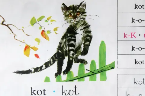 Ilustracja z książeczki do nauki czytania: kot siedzi na płotku, obok gałązka z liśćmi. Tekst "ala ma kota" i słowo "kot" powtarzają się.