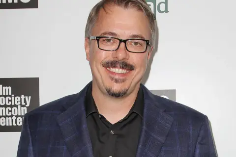 Vince Gilligan, twórca filmów, seriali i programów, w garniturze i okularach, uśmiecha się na tle logo "Film Society Lincoln Center" i symbolu pierwiastka "Br".