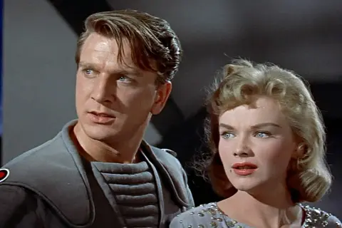 Leslie Nielsen w futurystycznym stroju obok kobiety w ozdobnej sukni, scena z jednego z jego filmów lub seriali.