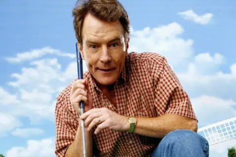 Bryan Cranston w kratę, z kijem golfowym, przypomina postać z jego filmów i seriali.