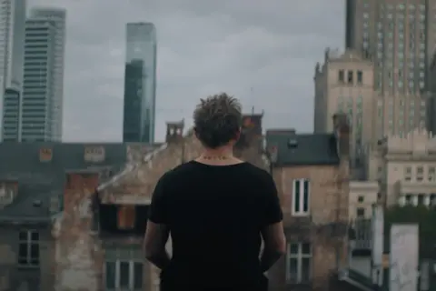 Młody mężczyzna z tatuażem "verte" na karku patrzy na panoramę Warszawy. Scena z serialu "Warszawianka".