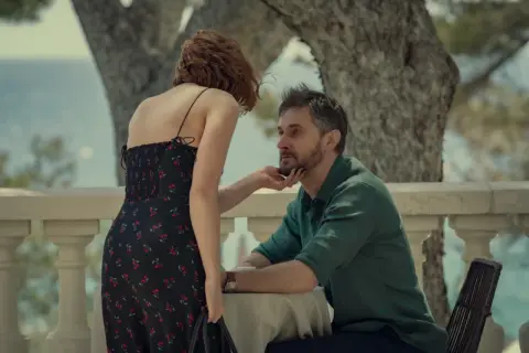 Kobieta w sukience w wiśnie dotyka brody mężczyzny. Napięcie między nimi sugeruje obsesję w tym serialu.