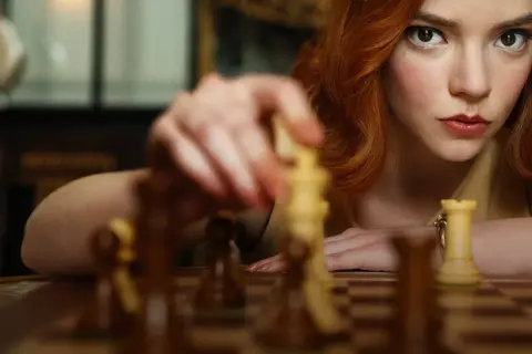 Beth Harmon, bohaterka "Gambitu królowej 2", skupiona na szachownicy, wykonuje ruch.