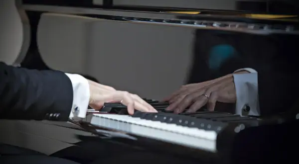 Dłonie muzyka w eleganckiej koszuli i garniturze grają najpiękniejsze utwory na fortepianie, tworząc magiczną melodię.