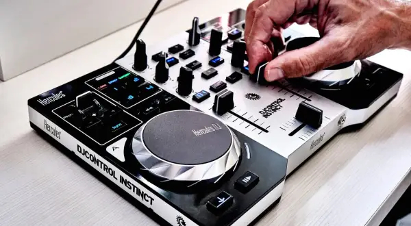 Dłoń DJ-a miksuje utwory na kontrolerze Hercules DJControl Instinct, tworząc energiczną muzykę do tańca.