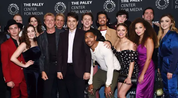 Uśmiechnięta cobra kai obsada pozuje do zdjęcia na tle logo The Paley Center for Media.