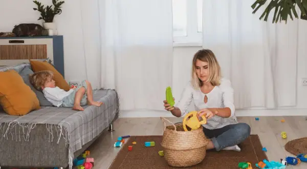 Filip leży na kanapie, a mama, która chyba zapomniała o porządku, siedzi na dywanie wśród zabawek.