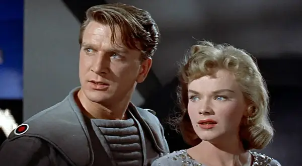 Leslie Nielsen w futurystycznym stroju obok kobiety w ozdobnej sukni, scena z jednego z jego filmów lub seriali.