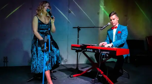 Wokalistka w niebieskiej sukience i pianista w garniturze tworzą duet. Ich występ to przykład kameralnych zespołów wokalnych.
