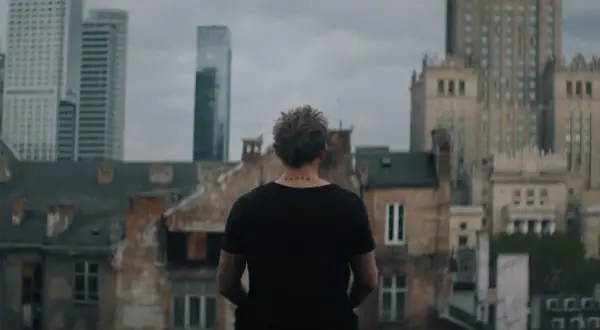 Młody mężczyzna z tatuażem "verte" na karku patrzy na panoramę Warszawy. Scena z serialu "Warszawianka".