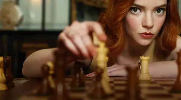 Beth Harmon, bohaterka "Gambitu królowej 2", skupiona na szachownicy, wykonuje ruch.