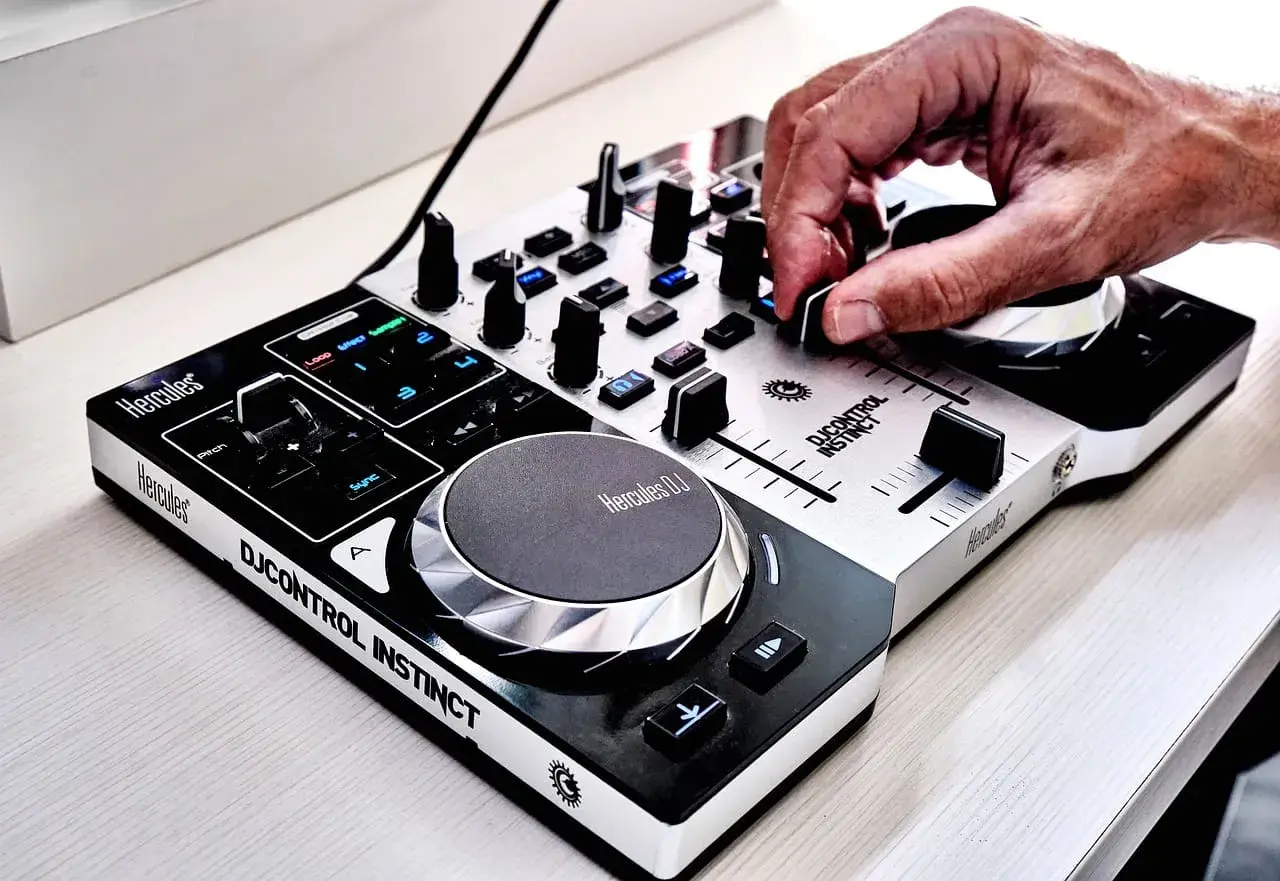 Dłoń DJ-a miksuje utwory na kontrolerze Hercules DJControl Instinct, tworząc energiczną muzykę do tańca.