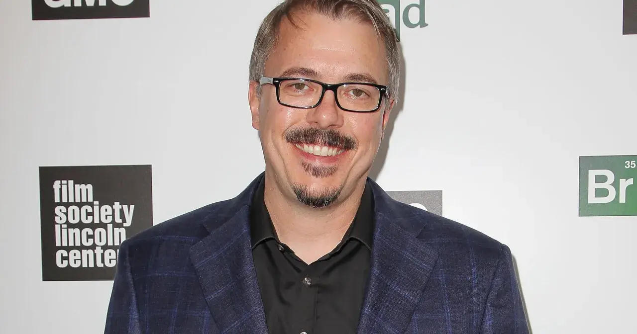 Vince Gilligan, twórca filmów, seriali i programów, w garniturze i okularach, uśmiecha się na tle logo "Film Society Lincoln Center" i symbolu pierwiastka "Br".
