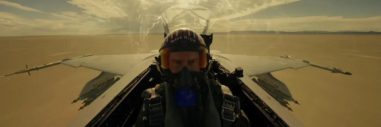 Pilot w hełmie "Maverick" w kokpicie myśliwca, gotowy do akcji. Scena jak z najlepszych filmów o lotnictwie.
