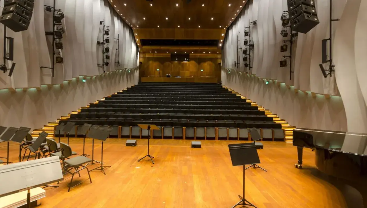 Pusta sala kameralna NOSPR z rzędami czarnych foteli, fortepianem i pulpitami dla muzyków.