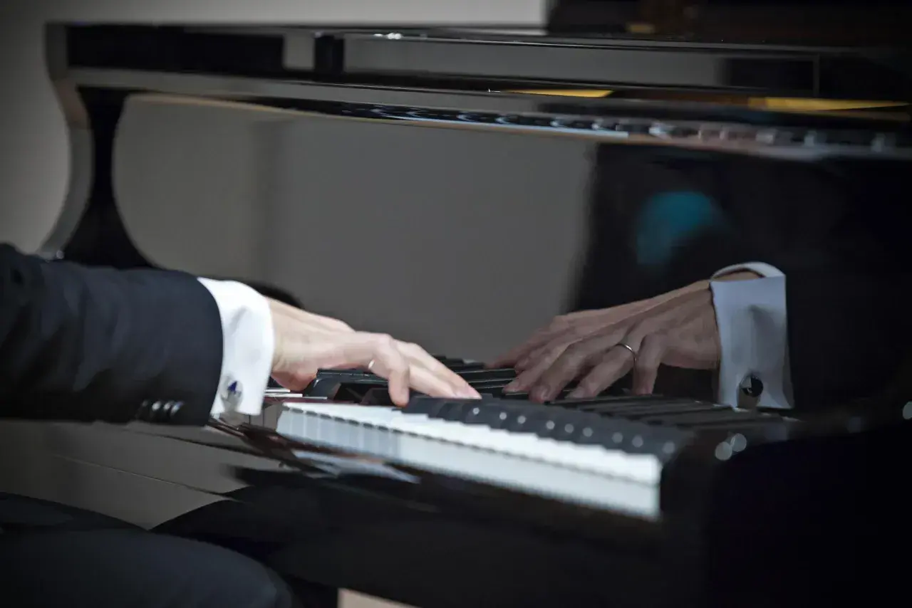 Dłonie w mankietach koszuli grają na fortepianie. W odbiciu widać drugiego pianistę. W tej chwili tworzą muzykę, jak prawdziwi sławni pianiści.