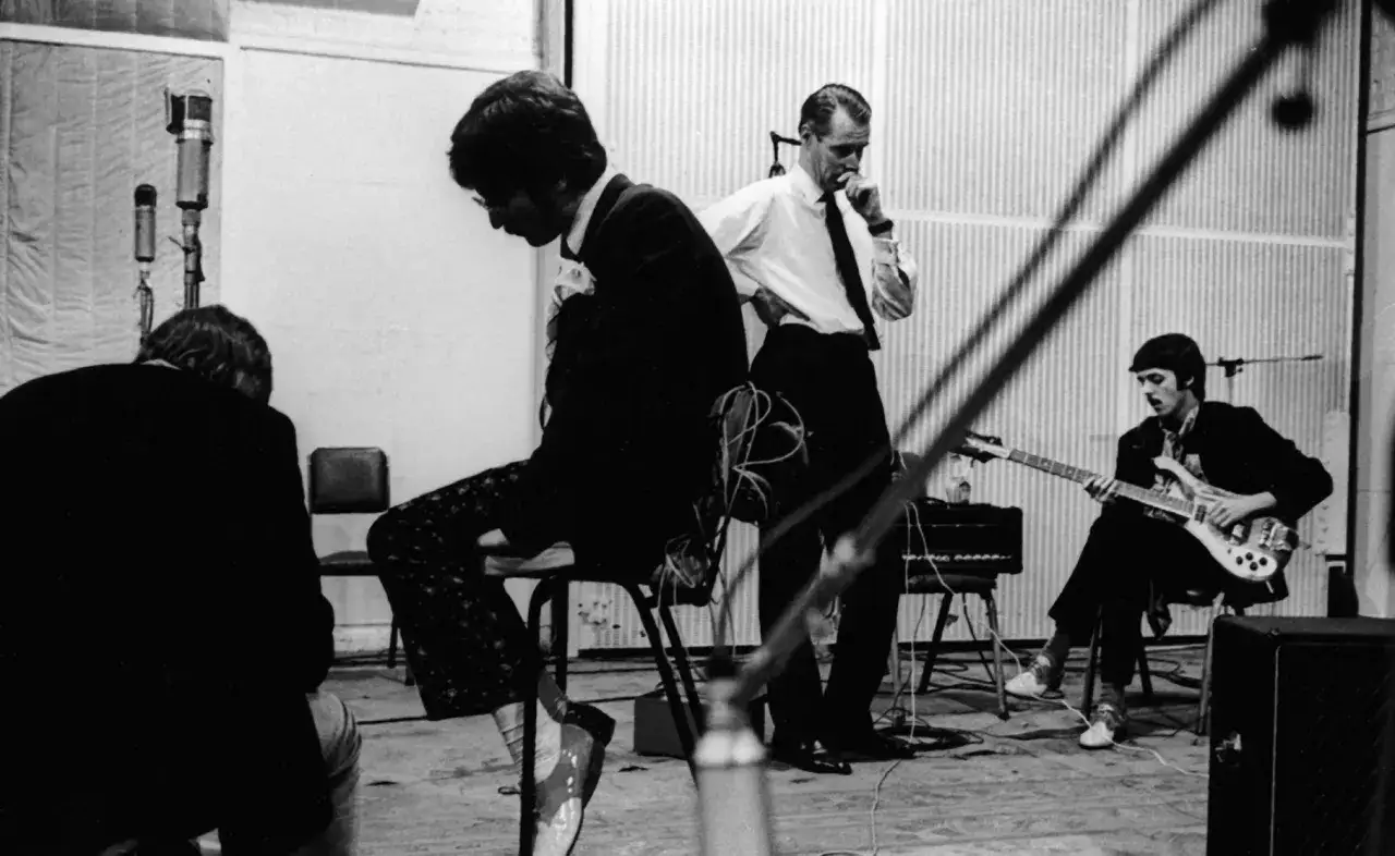 W studiu nagraniowym George Martin nadzoruje pracę The Beatles. Paul McCartney gra na gitarze, a John Lennon siedzi zamyślony.