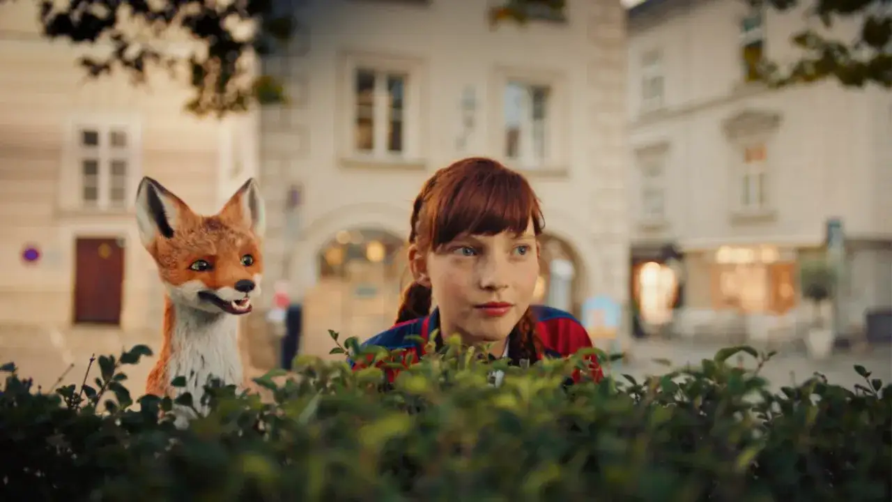 Rudowłosa dziewczynka i lis ukrywają się za krzakami. Scena z filmu