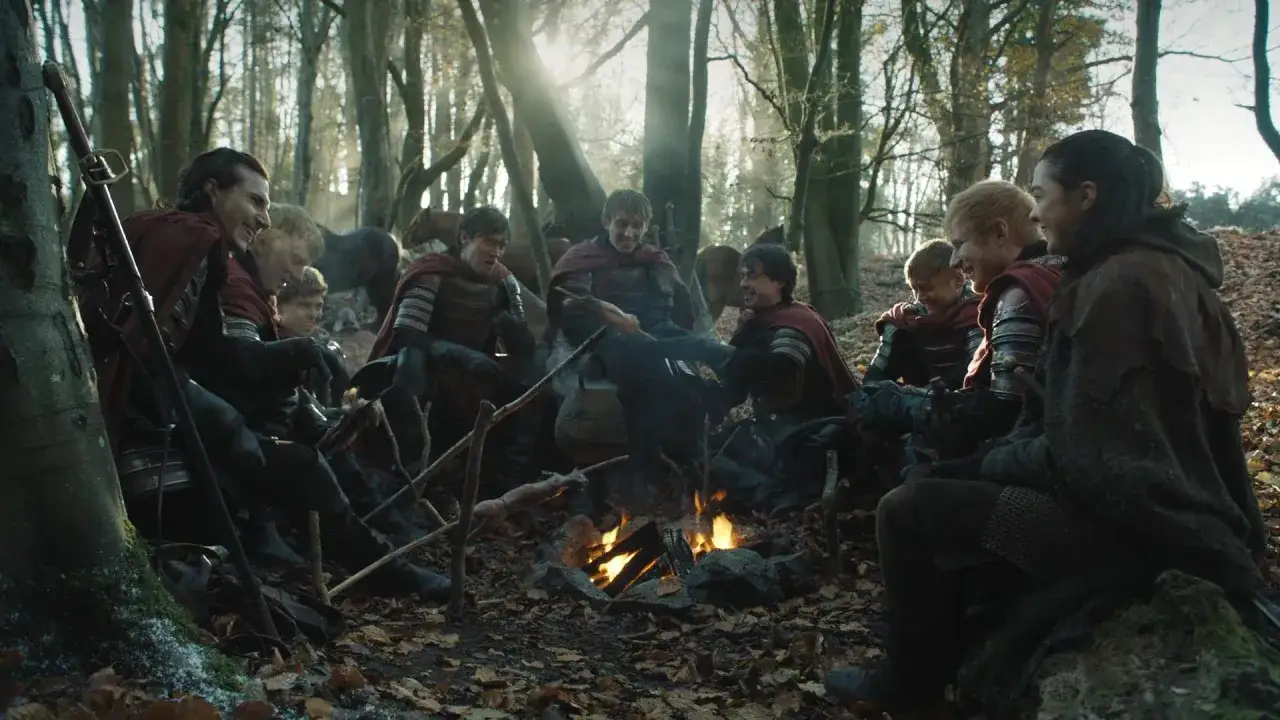 Ed Sheeran w stroju z Gry o Tron, siedzi przy ognisku z innymi żołnierzami w lesie.