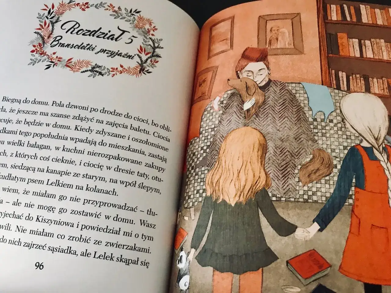 Ilustracja z książki: wiłka smocza dziewczynka trzyma za rękę drugą dziewczynkę, siedzącą obok cioci z psem.