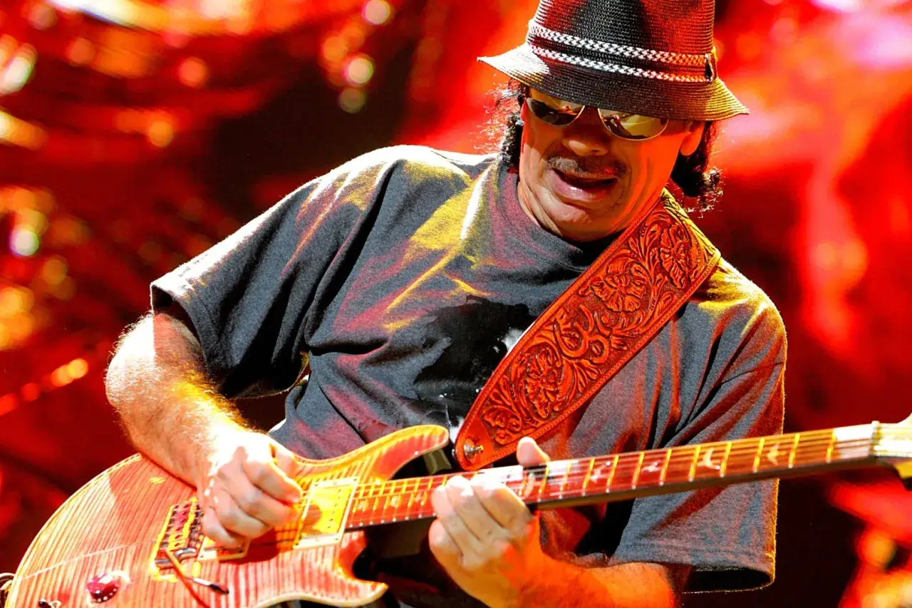 Carlos Santana w kapeluszu i okularach gra na gitarze, wykonując najbardziej znany utw&oacute;r.