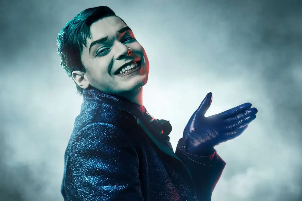 Cameron Monaghan w roli Jokera, znany z film&oacute;w i seriali, w błyszczącym garniturze i niebieskich rękawiczkach.