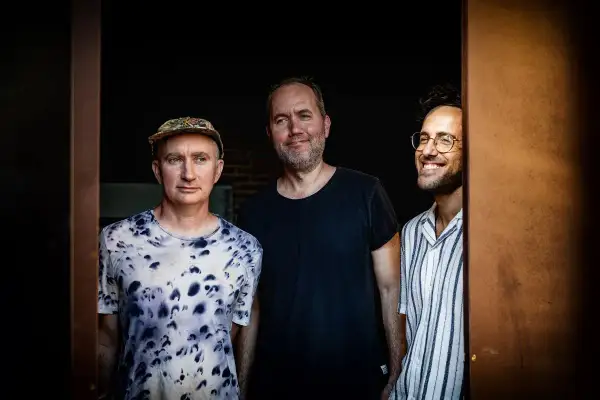 Trzech mężczyzn, muzycy, gotowi do improwizacji w ekspresyjnym stylu jazzowym.