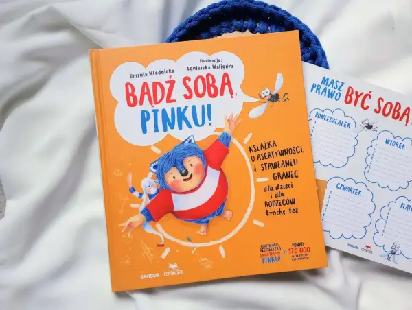 Pomarańczowa książka "Bądź sobą, Pinku!" z jeżem i zającem. Obok planer tygodniowy.