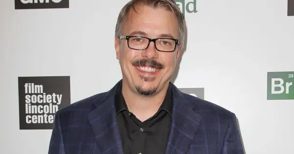 Vince Gilligan, twórca filmów, seriali i programów, w garniturze i okularach, uśmiecha się na tle logo "Film Society Lincoln Center" i symbolu pierwiastka "Br".