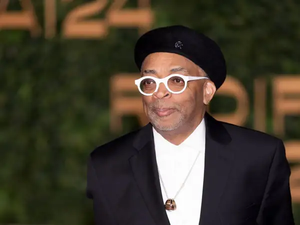 Spike Lee w czarnym beretce i białych okularach, od góry do dołu w czarnym garniturze i białej koszuli.