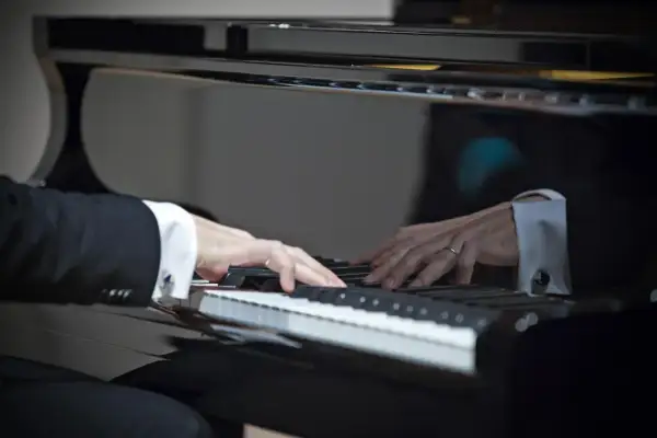 Dłonie w mankietach koszuli grają na fortepianie. W odbiciu widać drugiego pianistę. W tej chwili tworzą muzykę, jak prawdziwi sławni pianiści.